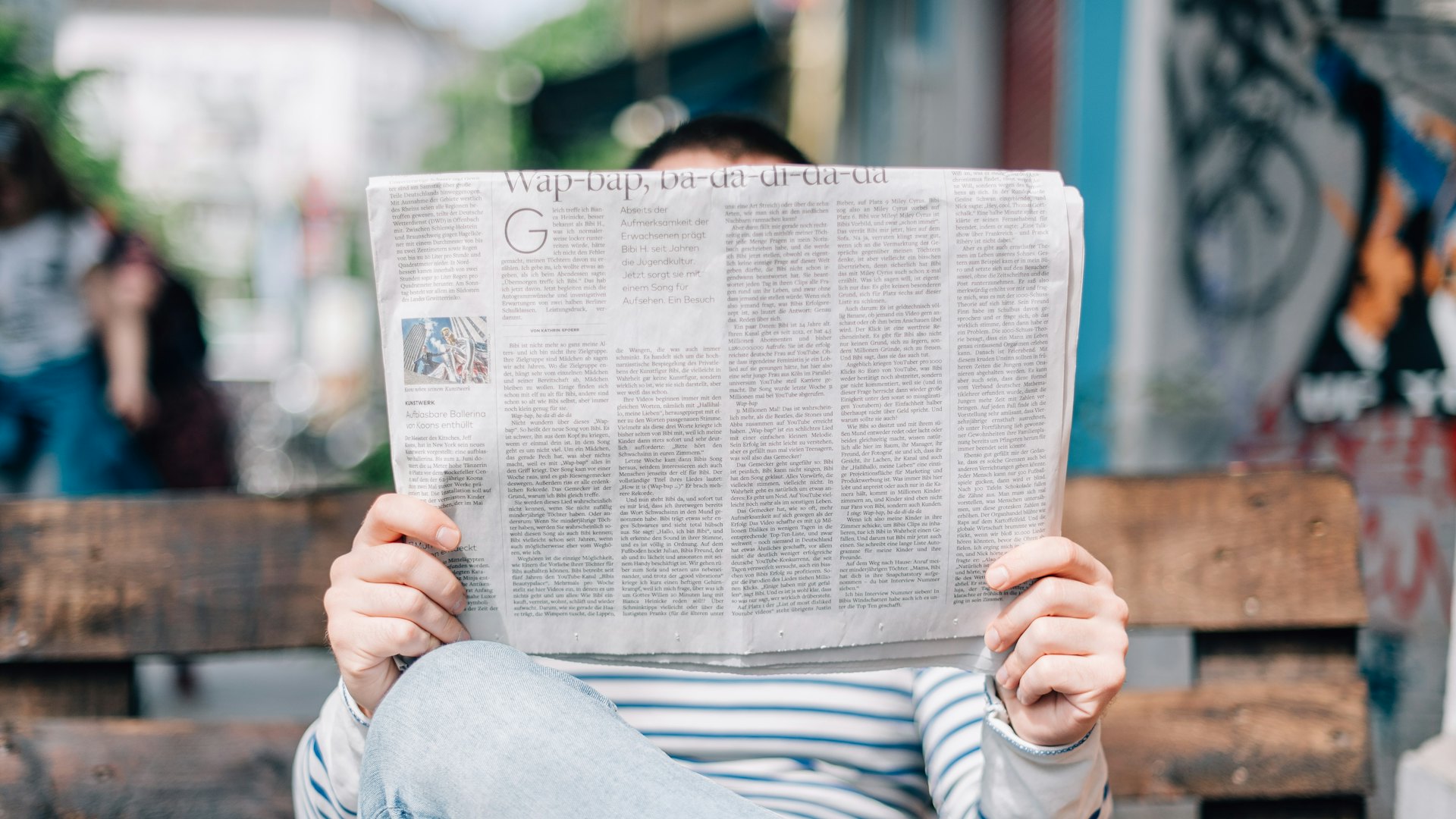 A reader catching up on the morning news with a newspaper on a city bench